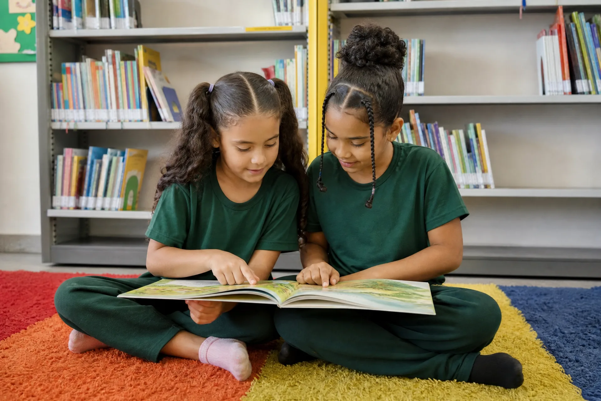 Duas alunas de uniforme lendo um livro na biblioteca da escola